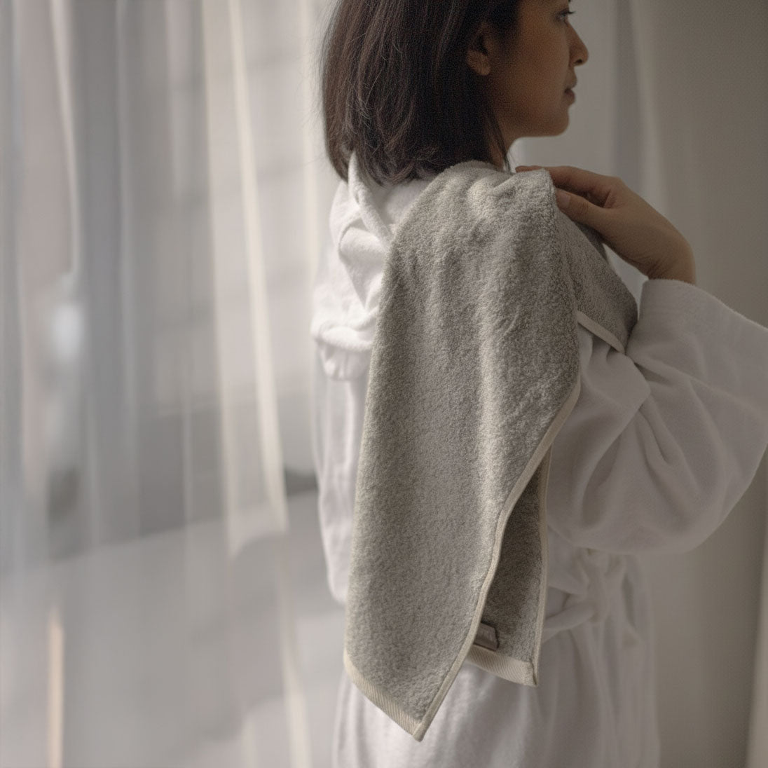 Person wearing a textured beige garment against a neutral background Holding Bulbul Copper Hand Towel.
