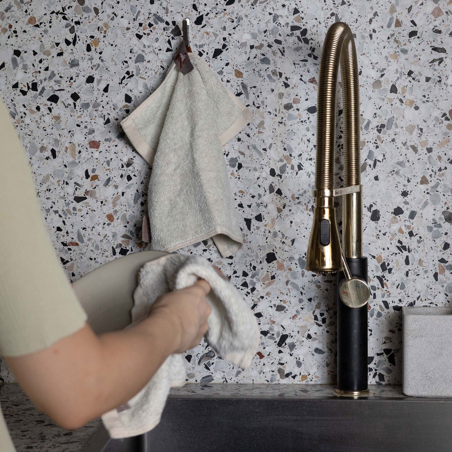 Bulbul Self-sanitizing Premium Copper Face Towel hanging near a modern kitchen sink with terrazzo backsplash. Antibacterial and odour-resistant design.