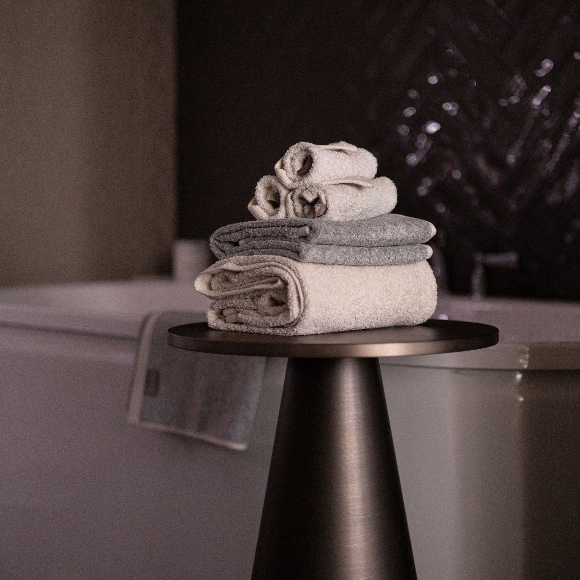 Bulbul Self-sanitizing Premium Copper Face Towel in beige and grey, neatly folded on a modern black stand beside a bathtub. Antibacterial and odour-resistant.