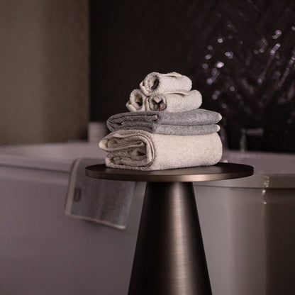 Bulbul Self-sanitizing Premium Copper Face Towel in beige and grey, neatly folded on a modern black stand beside a bathtub. Antibacterial and odour-resistant.